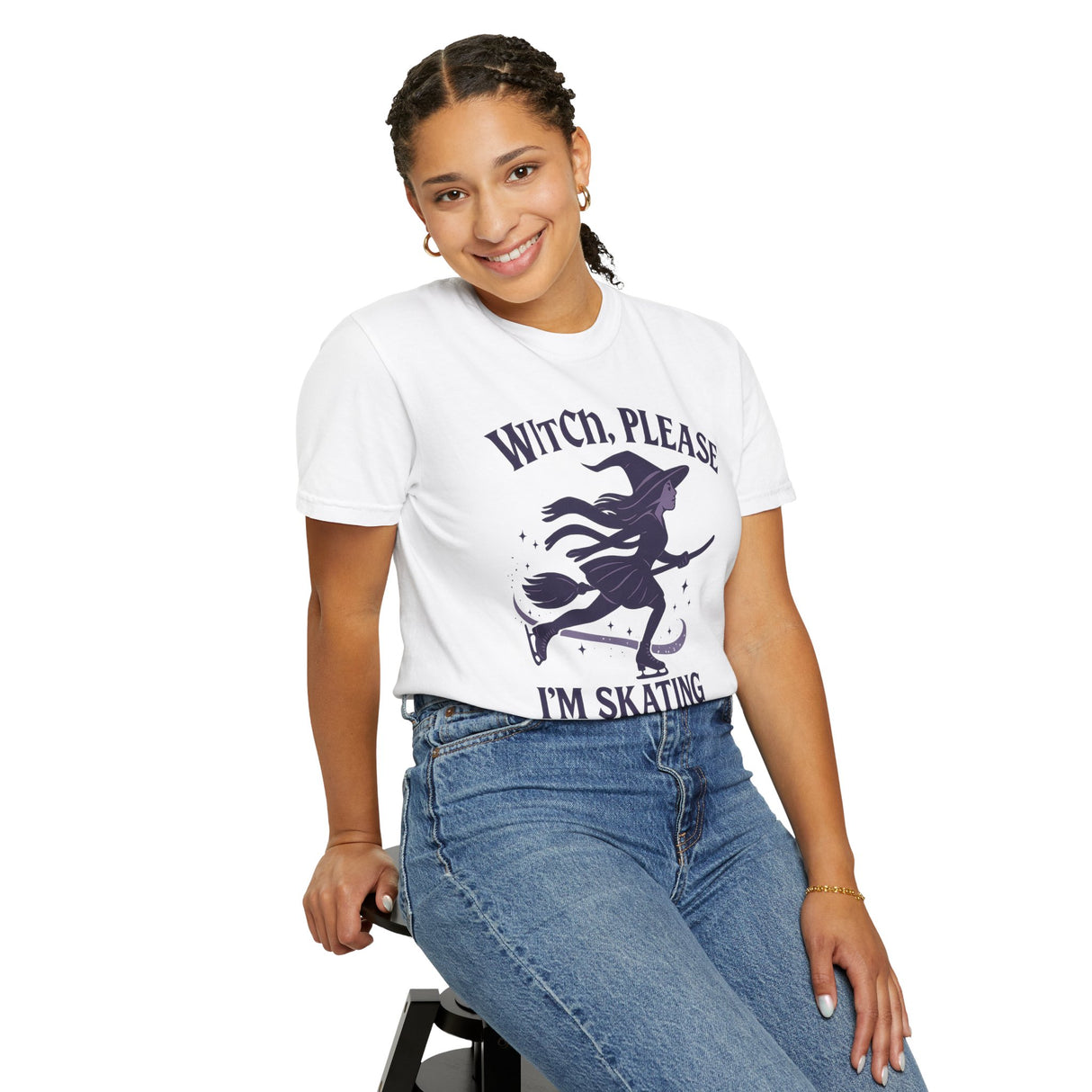 Person wearing a white t-shirt with a witch graphic and text, sitting on a stool against a white background.