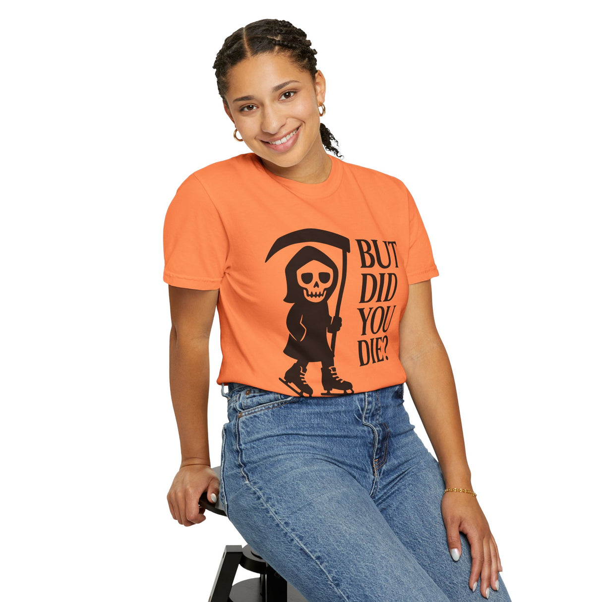 Person wearing an orange t-shirt with a graphic design and text, sitting on a stool against a white background.