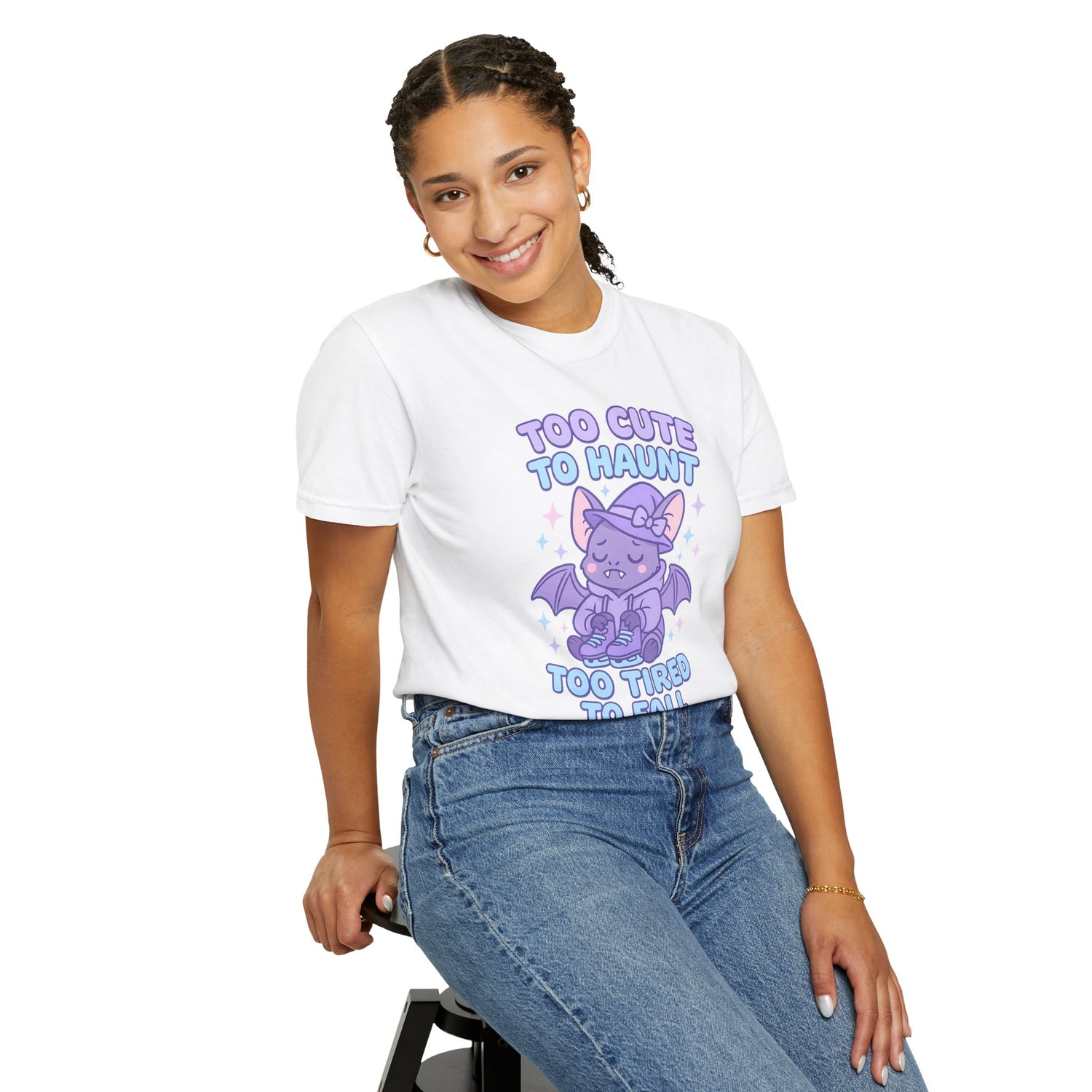 Person wearing a white t-shirt with a purple graphic and text, sitting on a stool against a white background