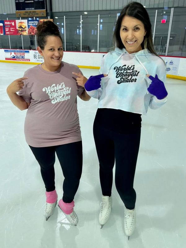Two skaters on the ice pointing at their World's Okayest Skater tee and tie-dye crop hoodie