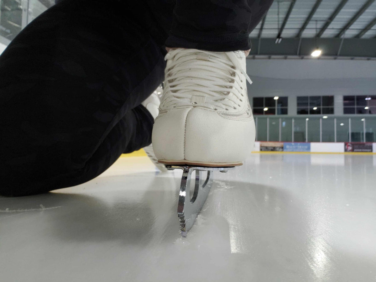 A figure skate on the ice, seen from blade level at the boards