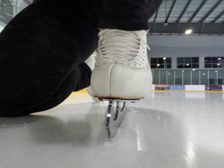 A figure skate on the ice, seen from blade level at the boards