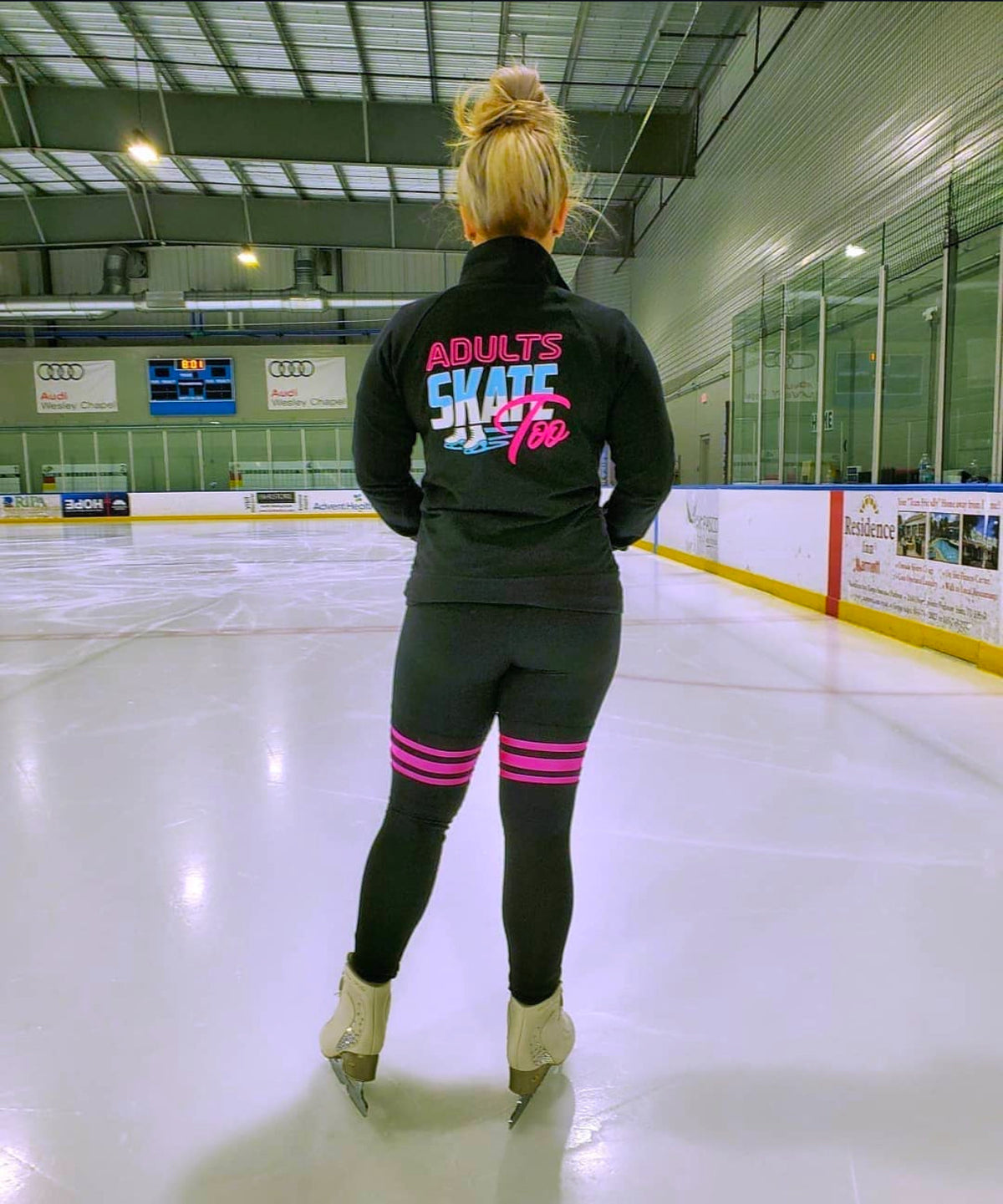 A skater seen from behind in an Adults Skate Too jacket, looking out across the ice.