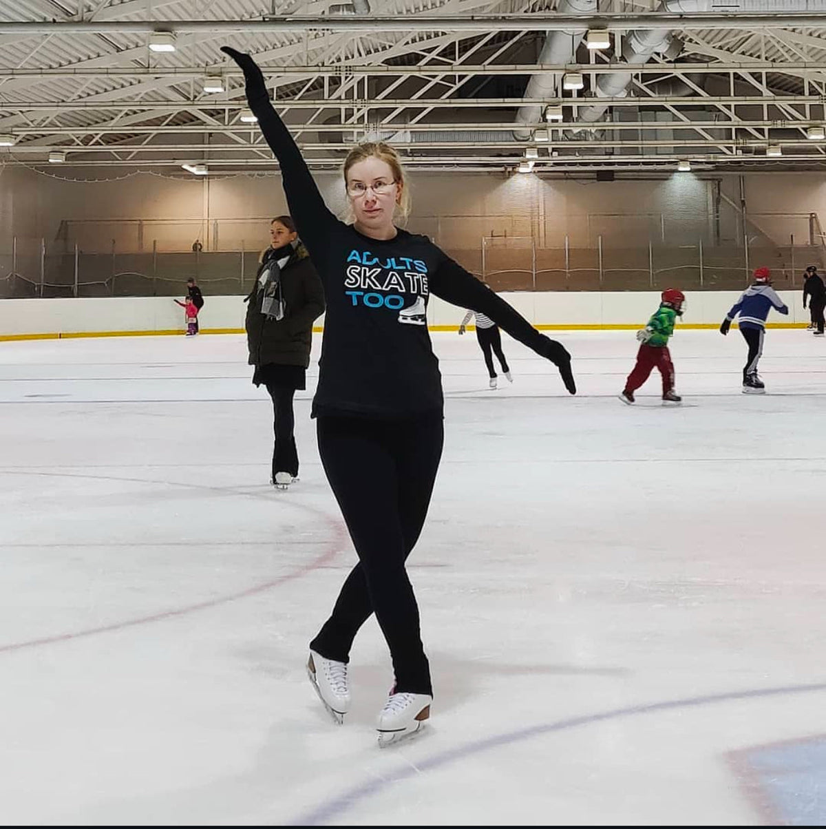 A skater in an Adults Skate Too shirt raising one arm during a busy public session.