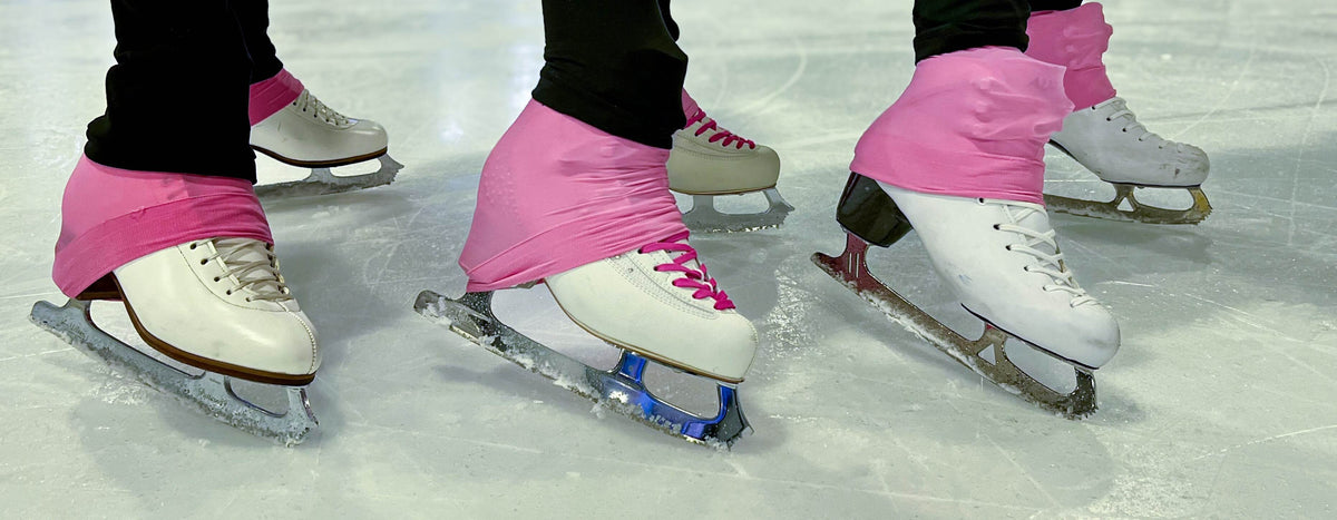 Skaters' feet in white figure skates with pink boot covers on the ice.