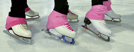 Skaters' feet in white figure skates with pink boot covers on the ice.