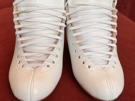 A pair of white figure skating boots, laced, on a red sofa