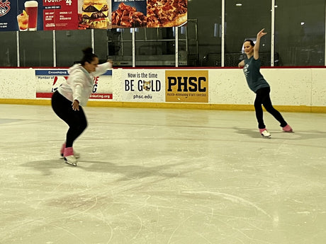 Two adult skaters stroking across a practice session at a rink