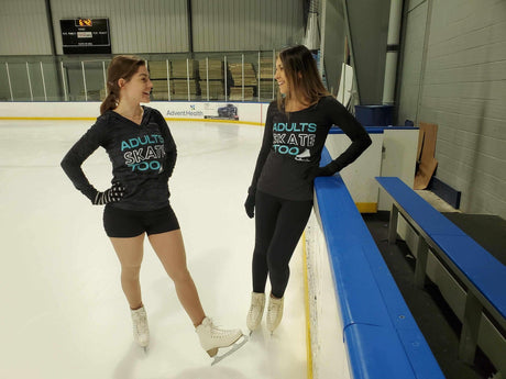 Two adult skaters in Adults Skate Too hoodies chatting at the rink boards