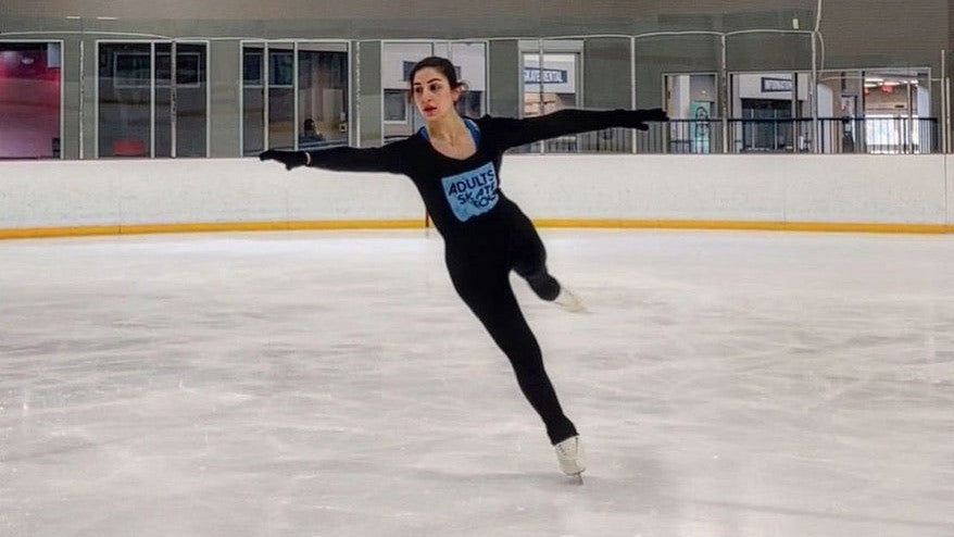 An adult skater in an Adults Skate Too tee gliding on one foot with her arms stretched out wide
