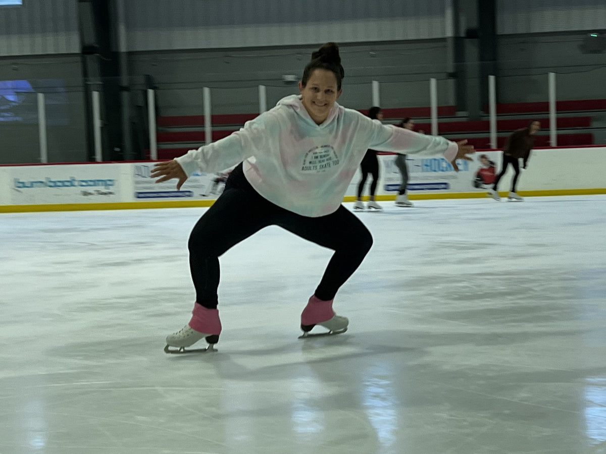 A skater holding a deep squat position on the ice, knees bent, arms out