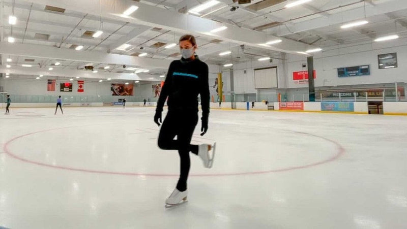 A skater gliding on one foot across a large, nearly empty rink