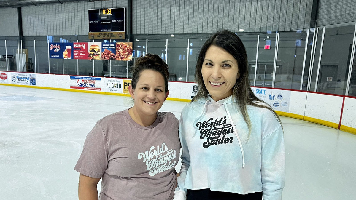 Two smiling skaters in printed tops standing together on an indoor rink.