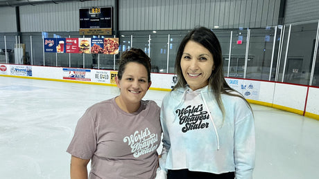 Two smiling skaters in printed tops standing together on an indoor rink.