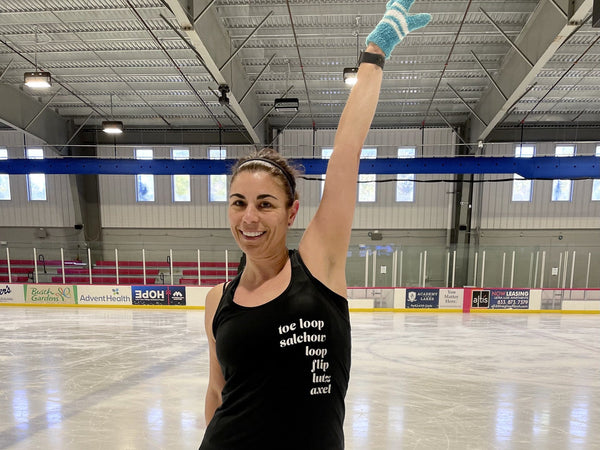 An adult skater on the ice with one arm raised, smiling