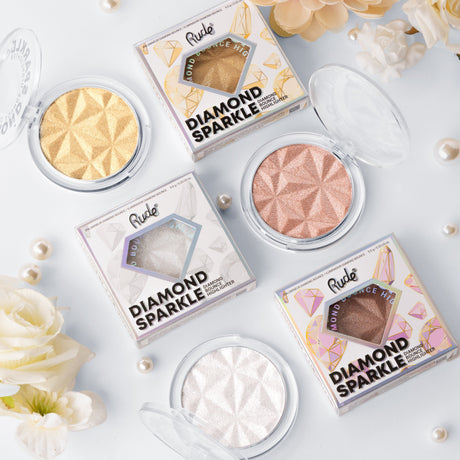 Rude Diamond Sparkle highlighter compacts in gold, rose and pearl shades laid out on white.
