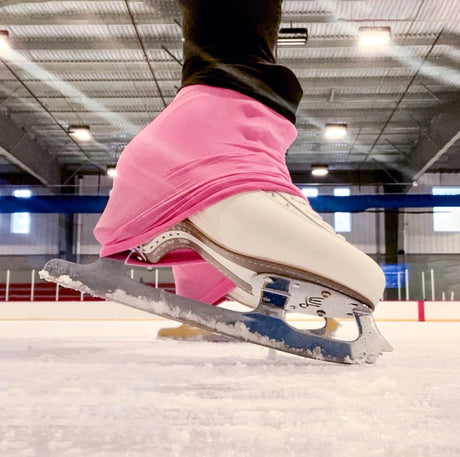 A white figure skate with a pink boot cover on the ice, seen up close.
