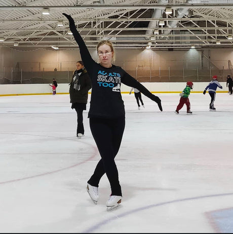 A skater in an Adults Skate Too shirt raising one arm during a busy public session.