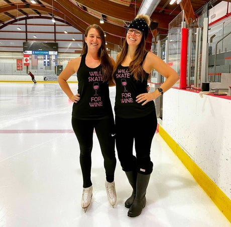 Two smiling skaters in Will Skate for Wine tanks standing at the rink boards.