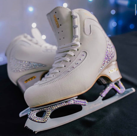 White figure skates with crystal-studded blades and heels on a black cloth.