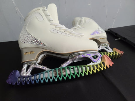 White figure skates with crystal detailing and rainbow blade guards on a black table.