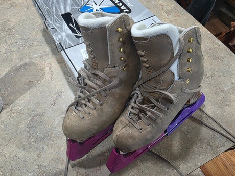 A pair of grey figure skates with purple blade guards on a counter.