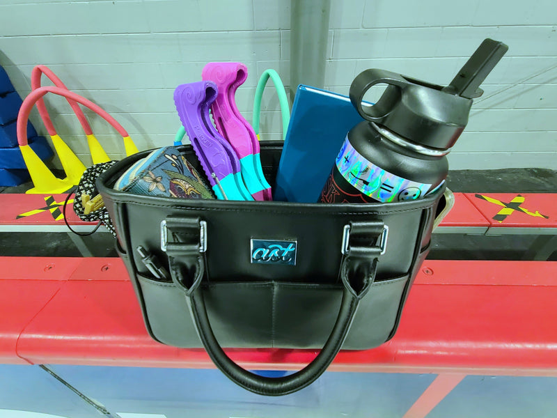 A black tote on the rink boards holding blade guards and a water bottle.