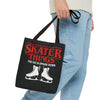 Black tote bag with red text and skates design held by a person wearing blue jeans.