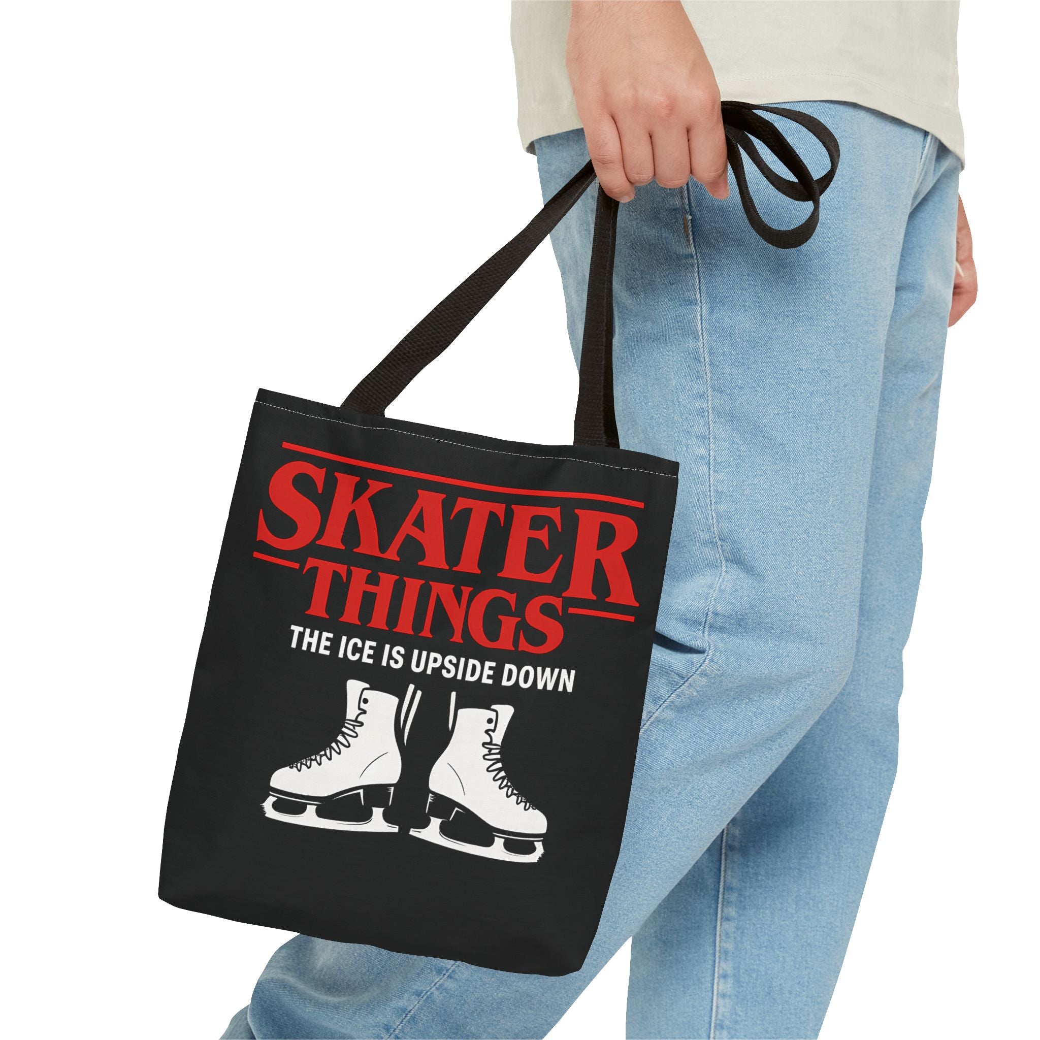 Black tote bag with red text and skates design held by a person wearing blue jeans.