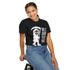 Person wearing a black t-shirt with a graphic design and text, sitting on a stool against a white background.