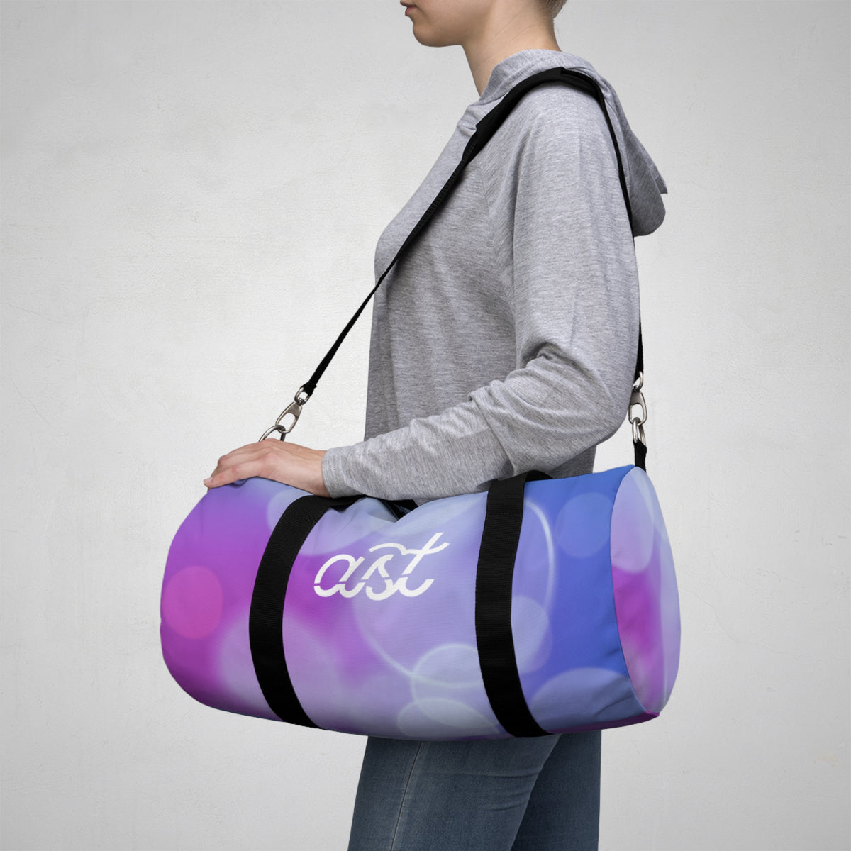 Person carrying a purple and blue duffel bag with 'ast' logo on a gray background