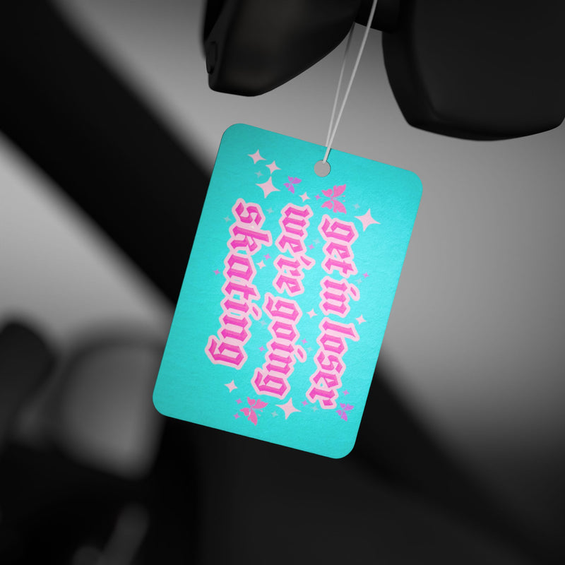 Turquoise car air freshener with pink text hanging from a car's rearview mirror.