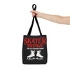 Black tote bag with red and white text and graphics, held by a hand on a white background