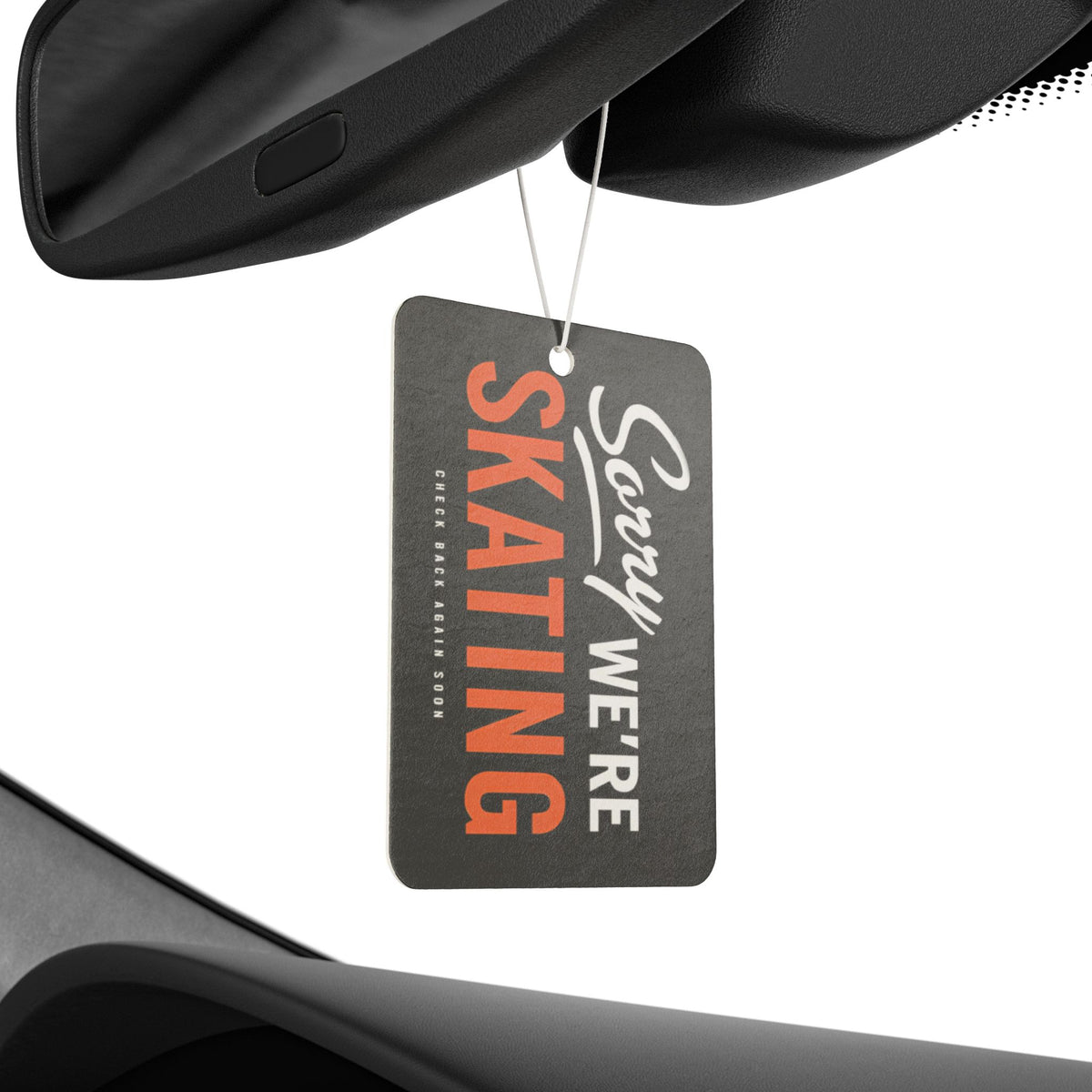Car air freshener with 'Sorry We're Skating' text hanging from a car's rearview mirror.