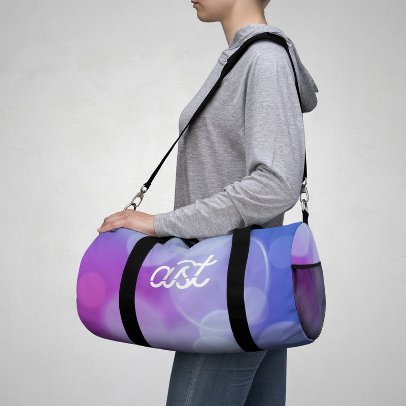Person carrying a purple and blue duffel bag with 'ast' branding on a gray background