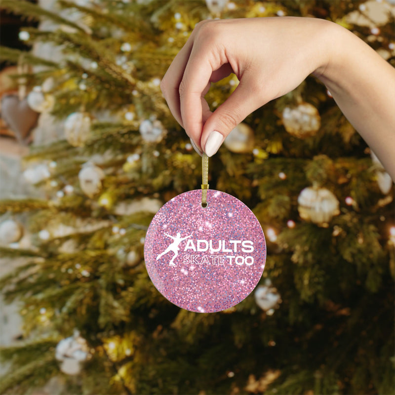 Pink glittery ornament with 'Adults Skate Too' text held by a hand in front of a decorated Christmas tree.