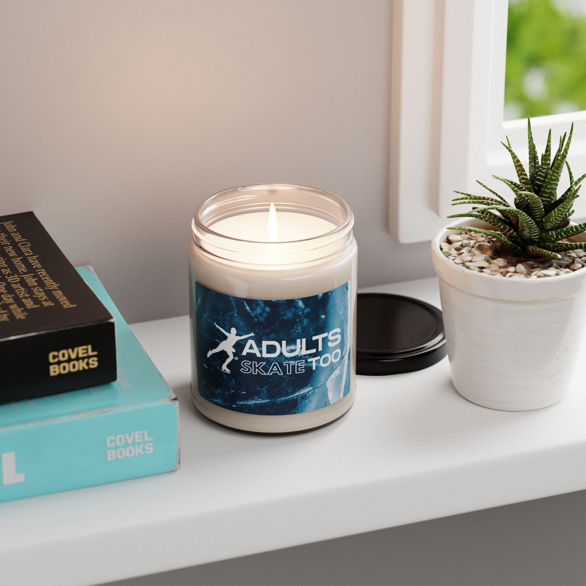 Candle with 'Adults Skate Too' design on a shelf with books and a plant