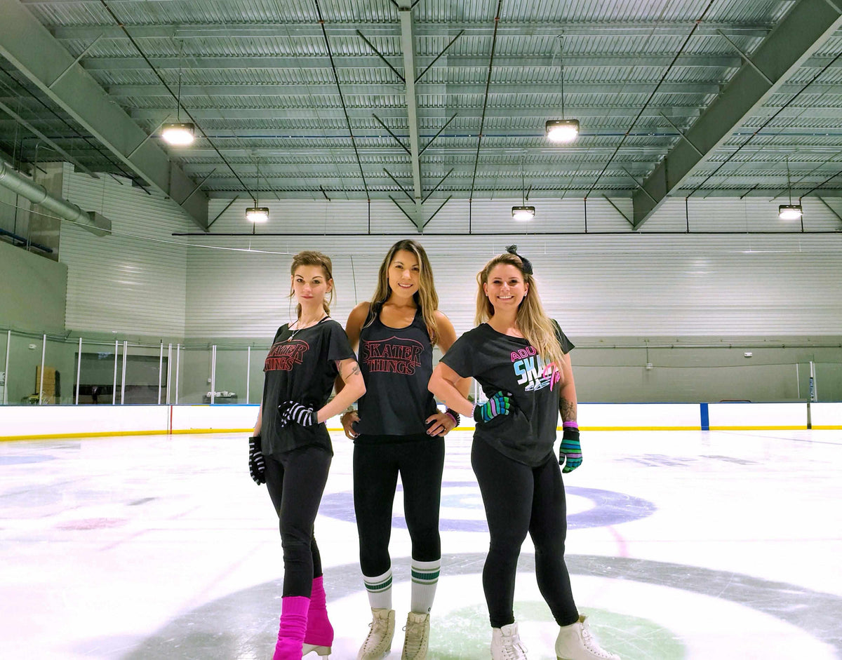 Three adult skaters in Adults Skate Too tees on the ice at the rink