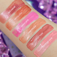 Lip gloss swatches on a hand with labeled colors against a purple glittery background