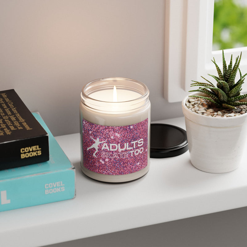 Candle with a pink glittery label on a shelf with books and a plant