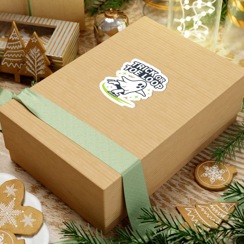 Wooden gift box with a green ribbon and 'Trick or Toop' sticker on a festive background with cookies and lights.