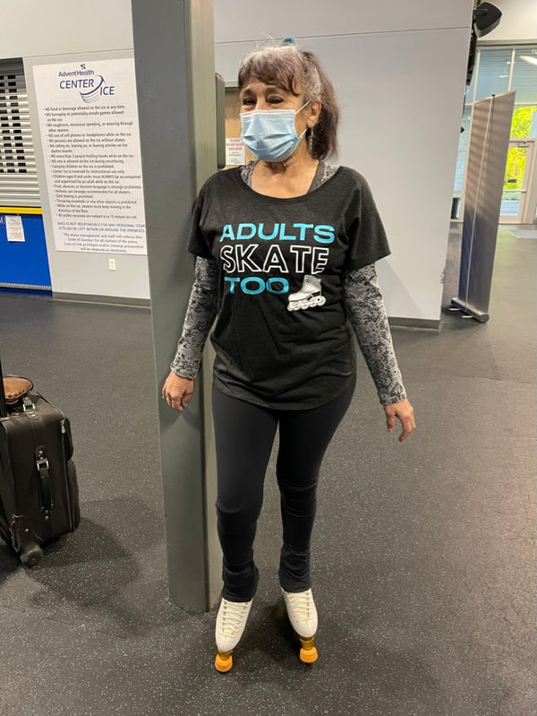 Masked skater on roller skates in a black Adults Skate Too tee, standing in a rink lobby