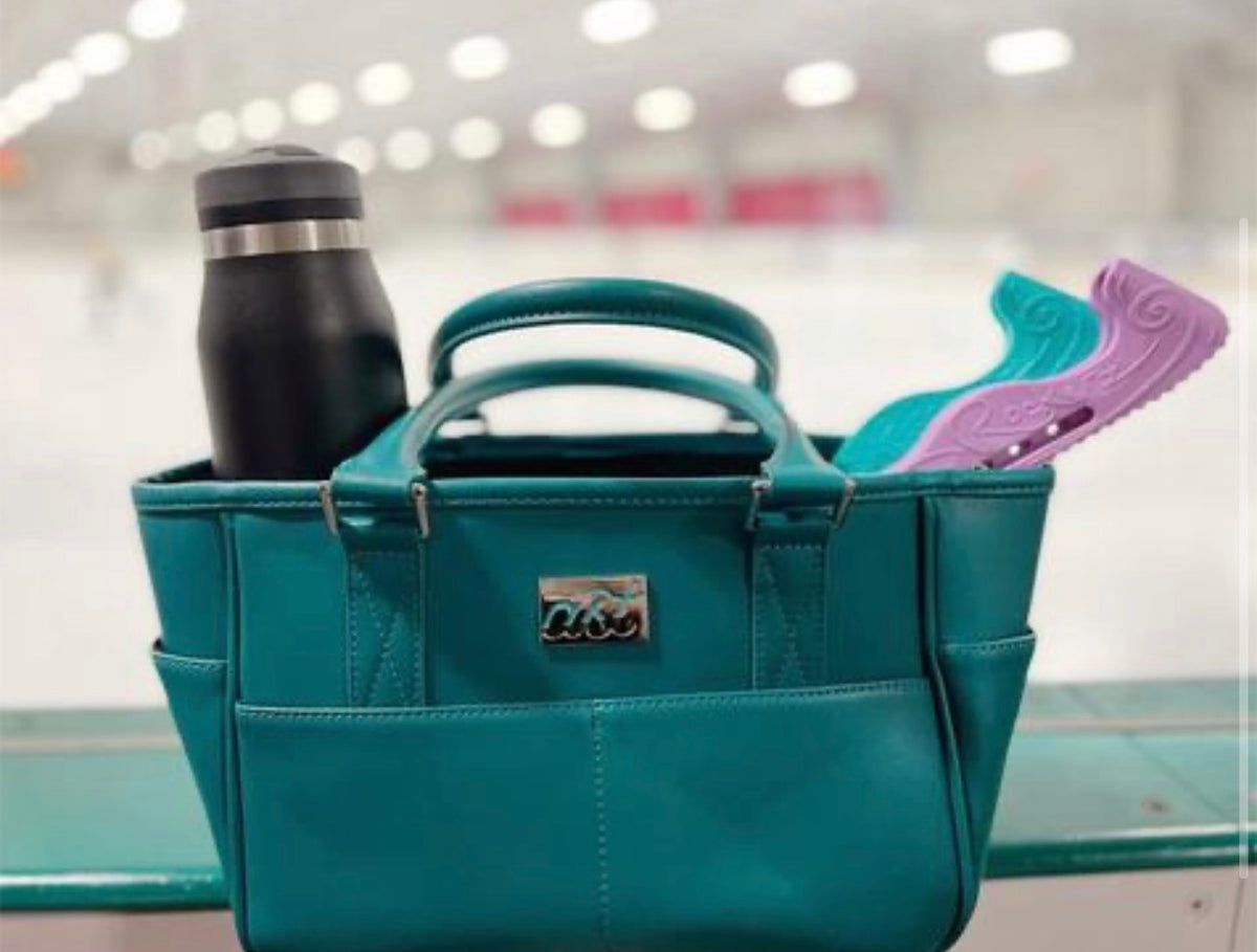 The teal Rink Side Tote packed with a water bottle and hard guards, sitting on the rink boards