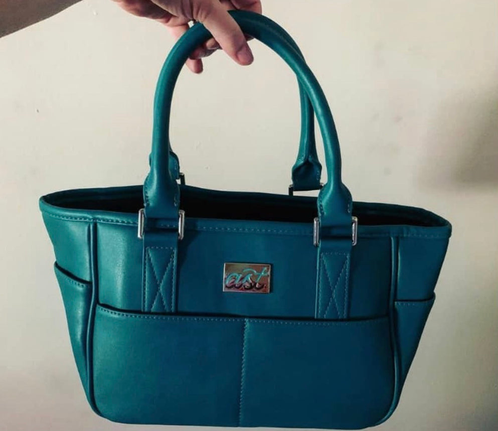 Teal handbag held by a hand against a plain background