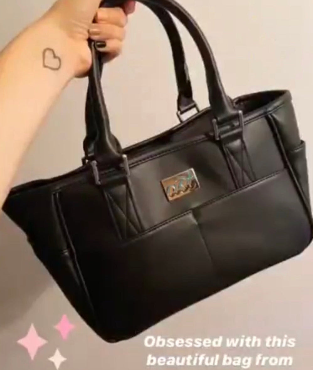 Black handbag held by a person with a neutral background