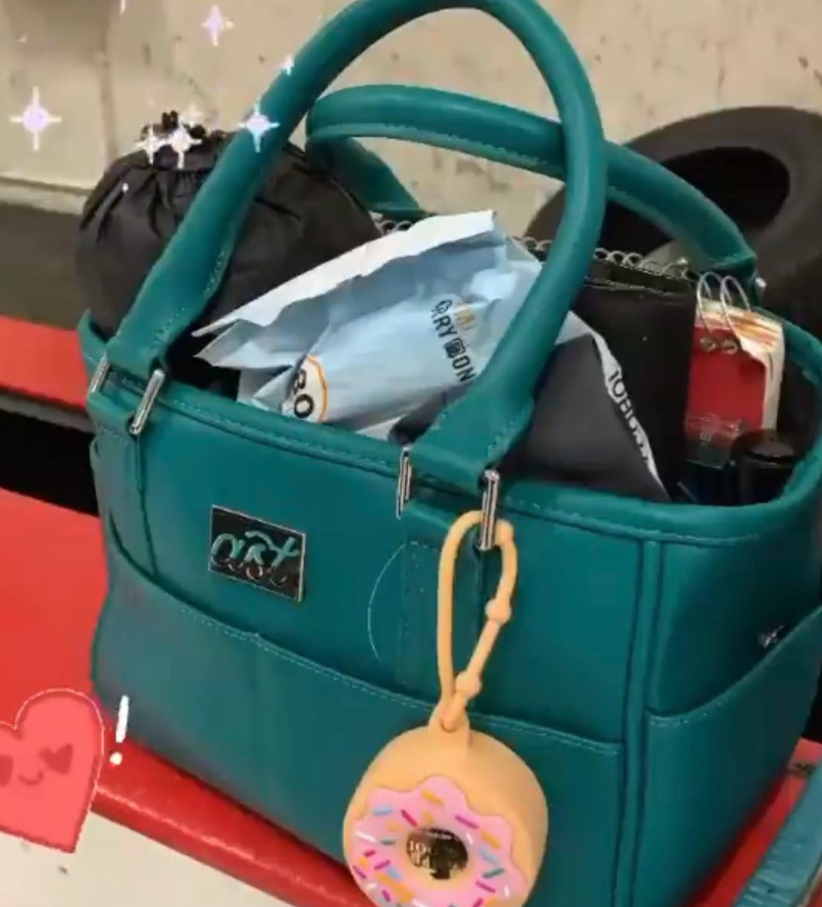Teal handbag with various items and a donut-shaped keychain on a red surface.