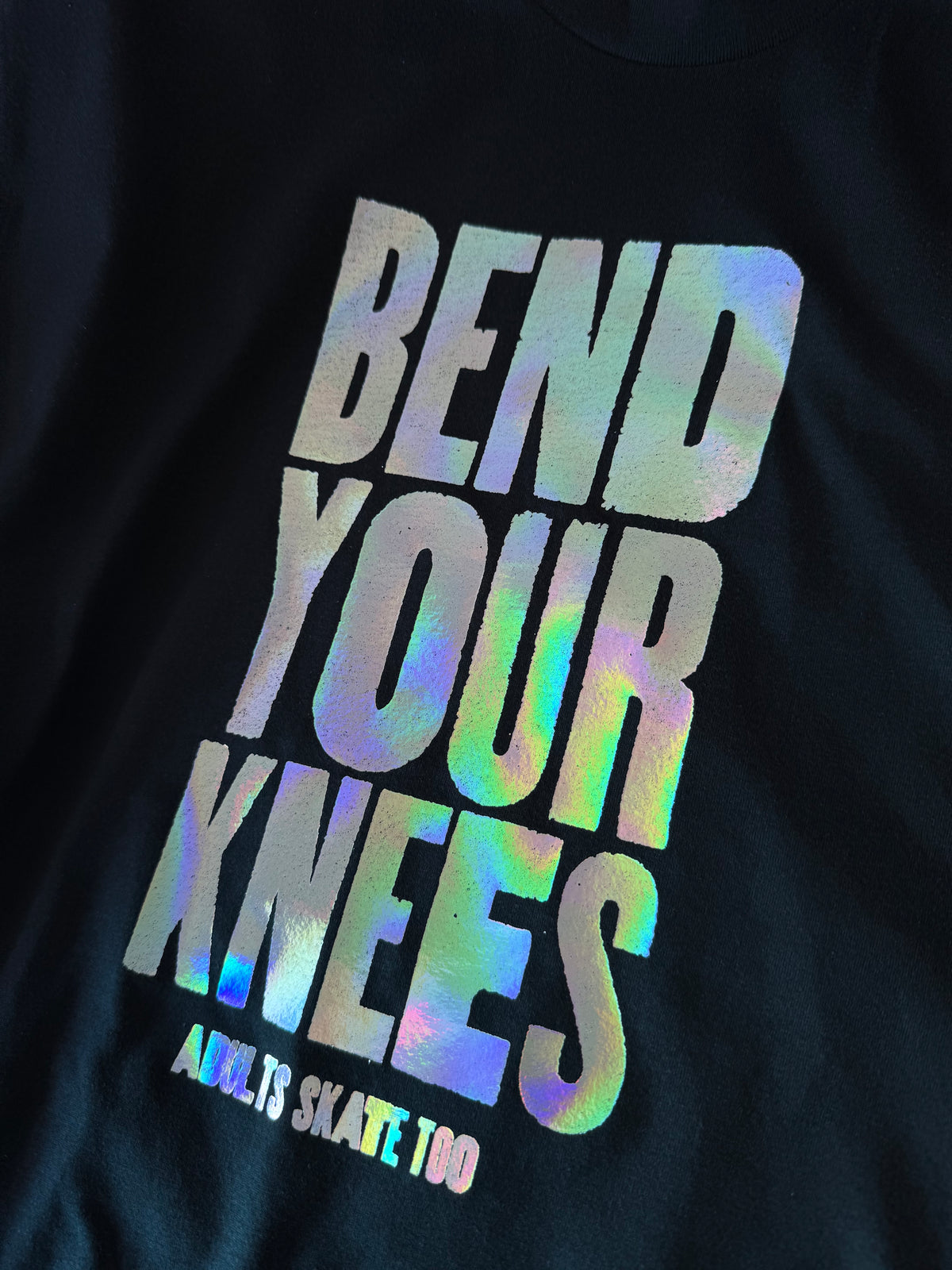A close-up of a holographic Bend Your Knees print on a black tee.