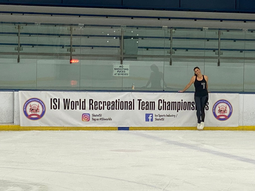 An adult skater in black leaning on the boards beside an ISI World Recreational Team Championships banner