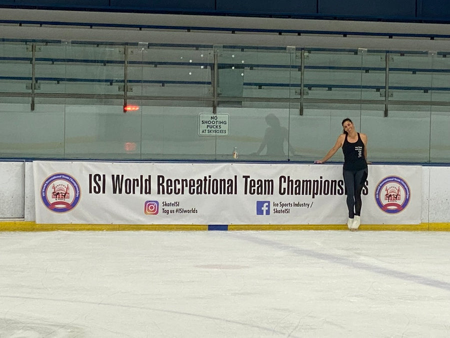 An adult skater in black leaning on the boards beside an ISI World Recreational Team Championships banner