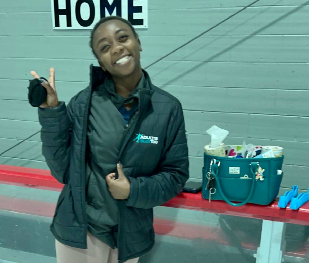 Person wearing a jacket with a logo, standing next to a teal bag and gloves on a red surface.